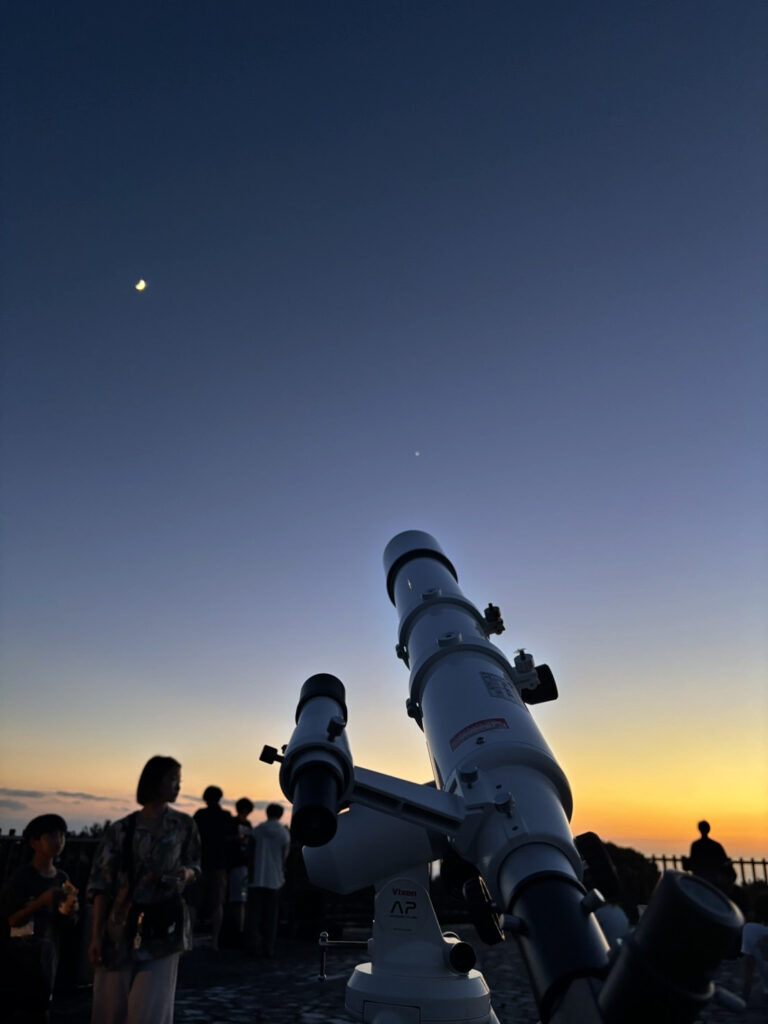 国頭村森林公園の展望台にて望遠鏡で金星、月、散開星団、二重星(アルビレオ)を観察している様子。